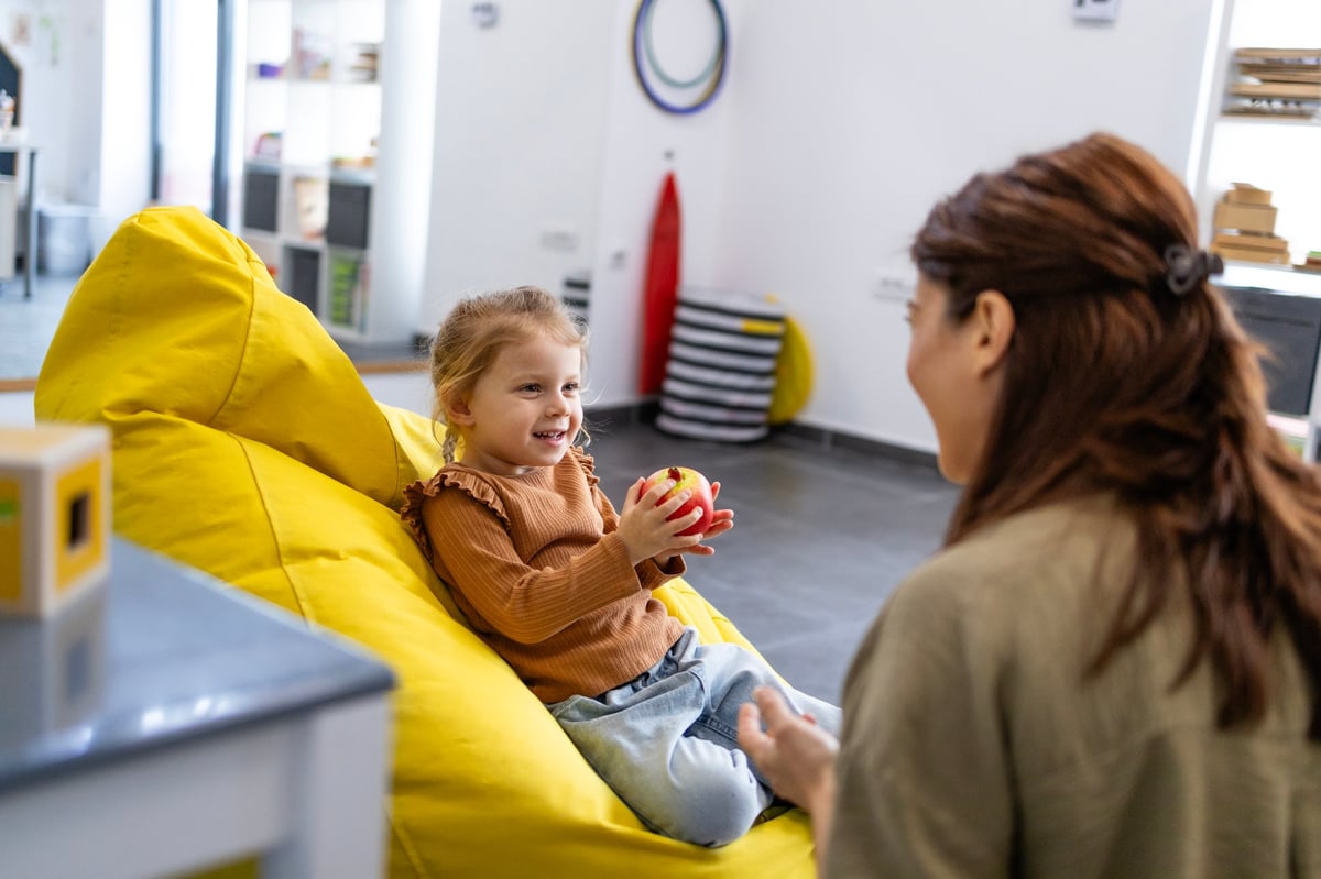 A young girl smiles while a caring therapist works with her in a bright, warm therapy session